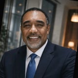 Professional headshot of a smiling man in a dark suit and blue tie against a blurred indoor background